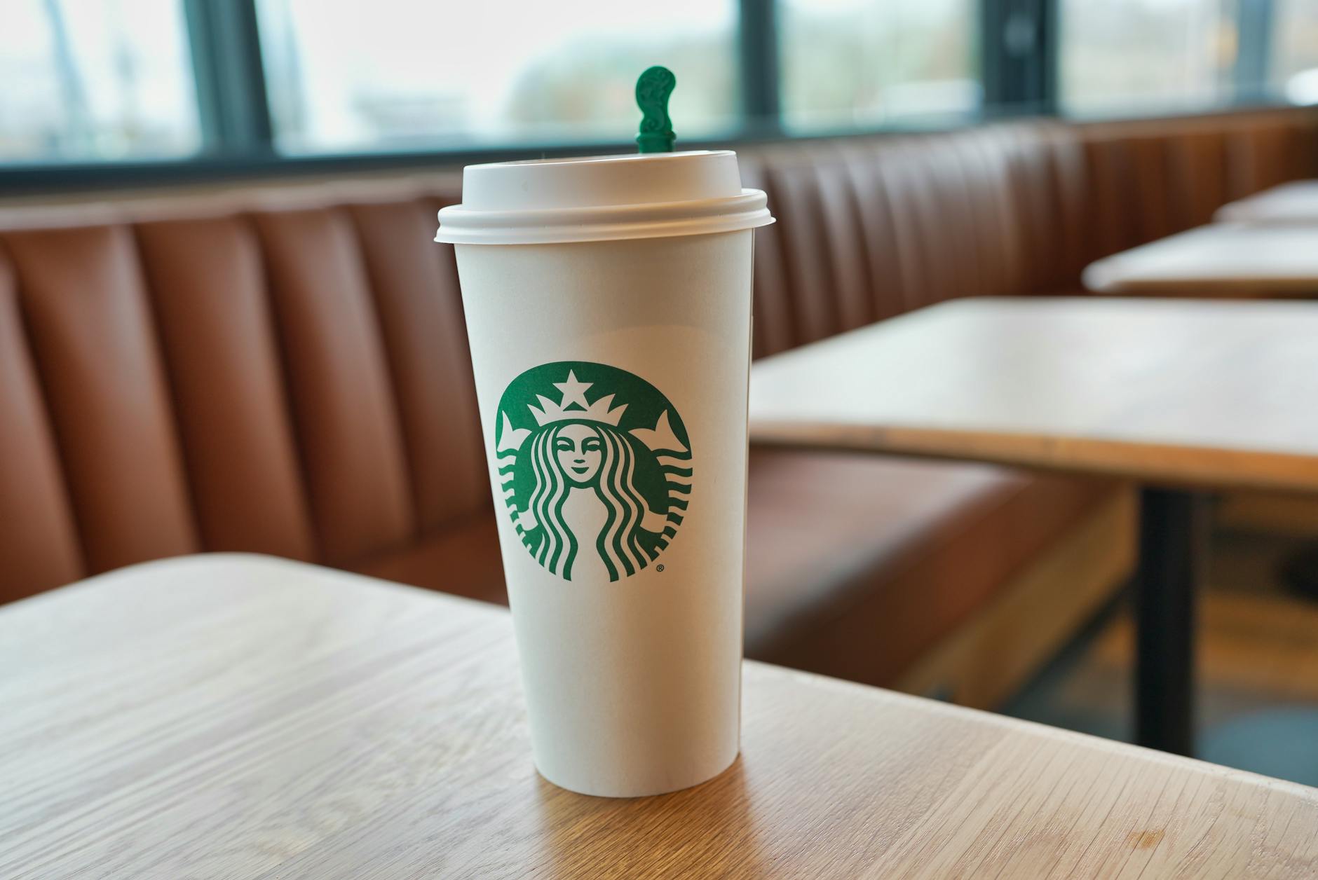 A Starbucks coffee cup on a wooden table inside a cafe, creating a cozy atmosphere.