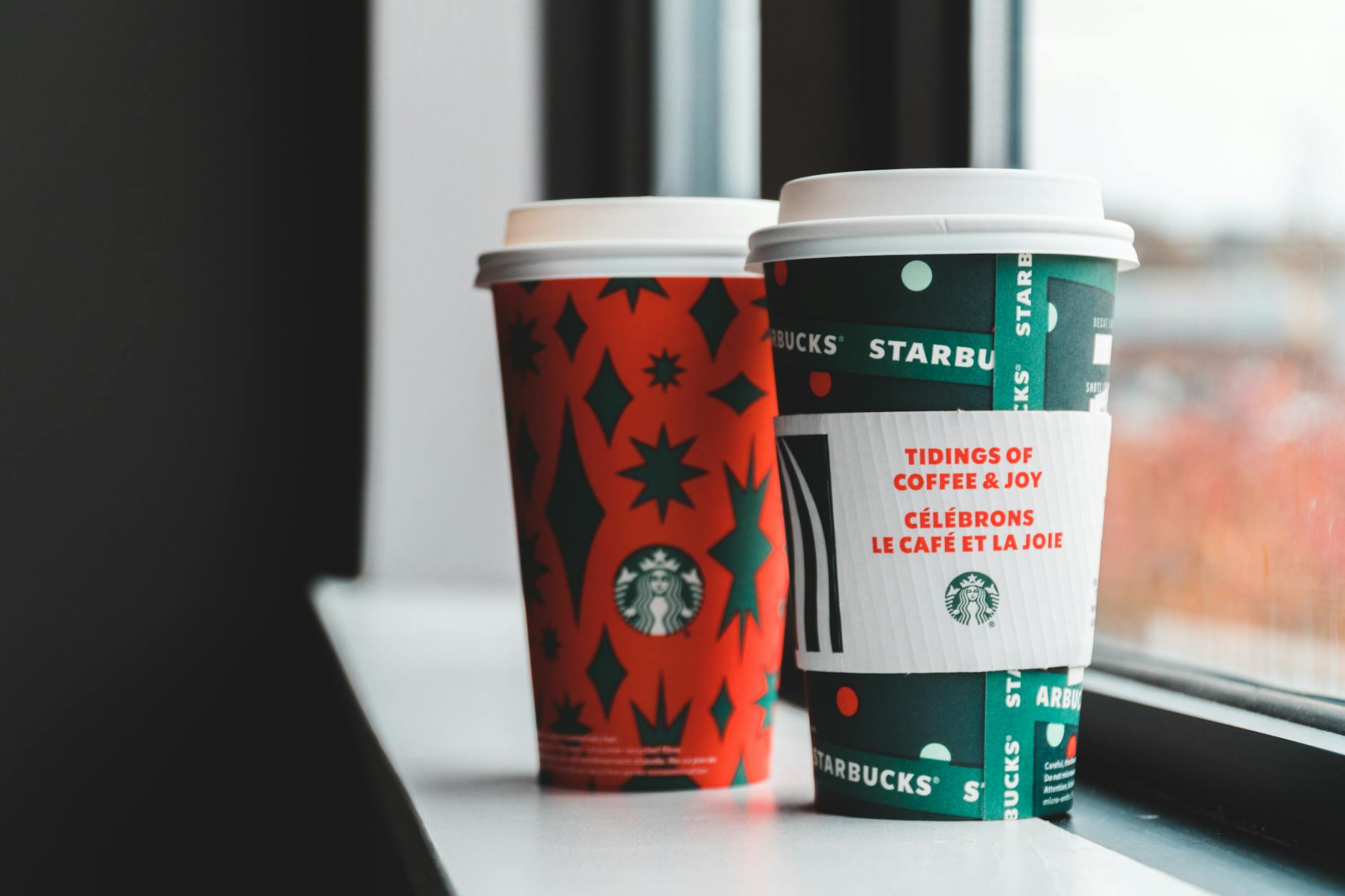 Festive Starbucks coffee cups with holiday designs on a windowsill. Perfect for cozy winter vibes.